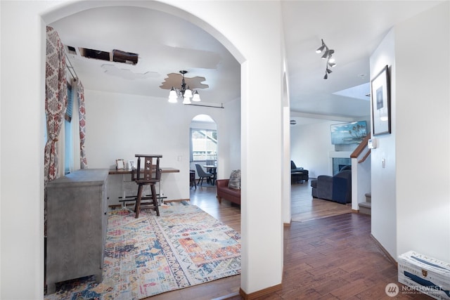 hall featuring arched walkways, wood finished floors, a chandelier, and stairs