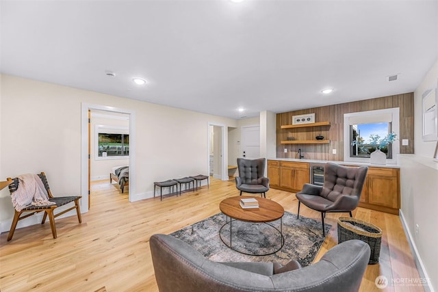 living room featuring wine cooler, indoor wet bar, baseboards, recessed lighting, and light wood-style flooring