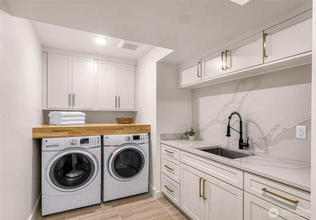 clothes washing area featuring washer and dryer, cabinet space, a sink, baseboards, and light wood-type flooring