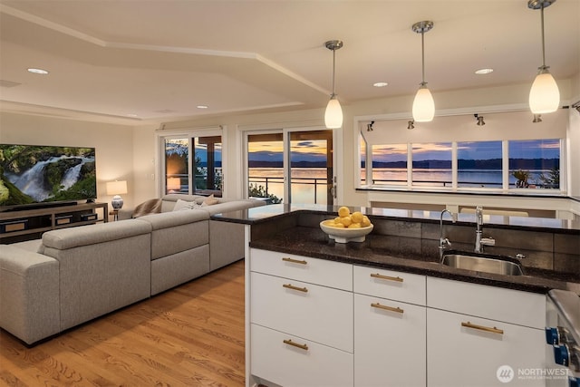 kitchen with light wood-type flooring, a sink, dark stone counters, open floor plan, and white cabinets