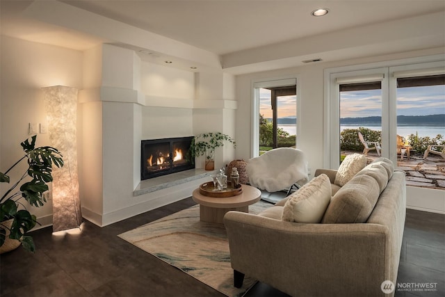 living area featuring a lit fireplace, recessed lighting, a water view, and baseboards