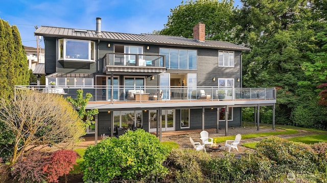 rear view of property featuring a standing seam roof, a chimney, an outdoor fire pit, a balcony, and metal roof