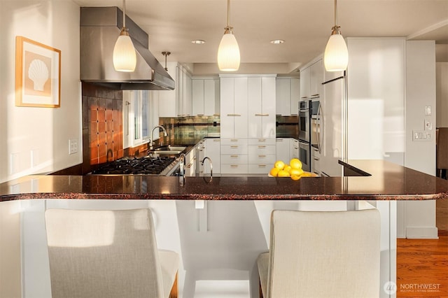 kitchen featuring island exhaust hood, a sink, gas cooktop, decorative backsplash, and a peninsula