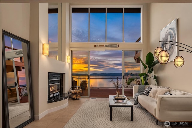 tiled living area with a towering ceiling, a water view, and a glass covered fireplace