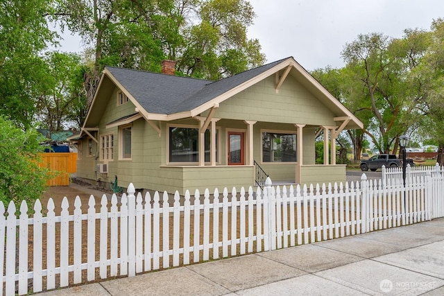 view of front of property featuring a chimney, a porch, roof with shingles, and a fenced front yard