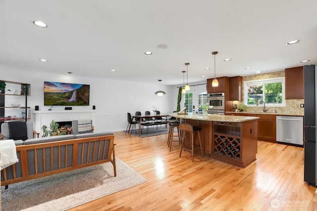 kitchen featuring appliances with stainless steel finishes, recessed lighting, light wood-type flooring, a warm lit fireplace, and tasteful backsplash
