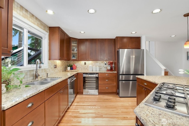 kitchen with appliances with stainless steel finishes, beverage cooler, a sink, light wood-style floors, and decorative backsplash