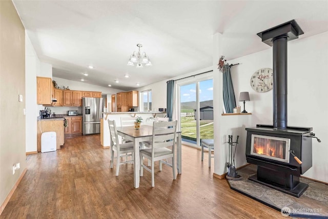dining space with an inviting chandelier, a wood stove, baseboards, wood finished floors, and lofted ceiling