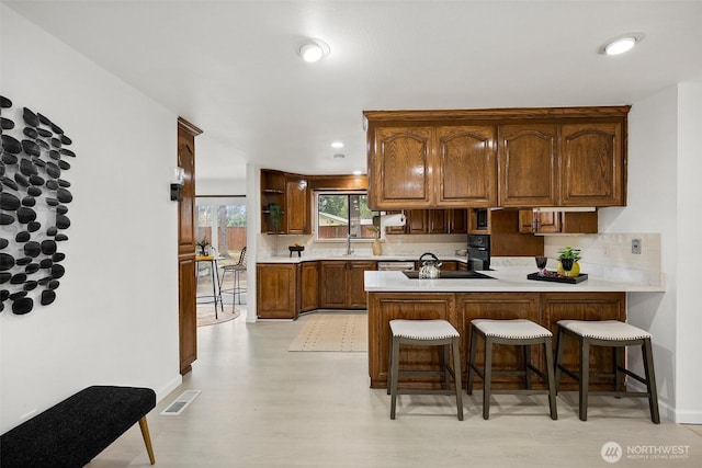 kitchen with light countertops, a breakfast bar area, a peninsula, backsplash, and visible vents