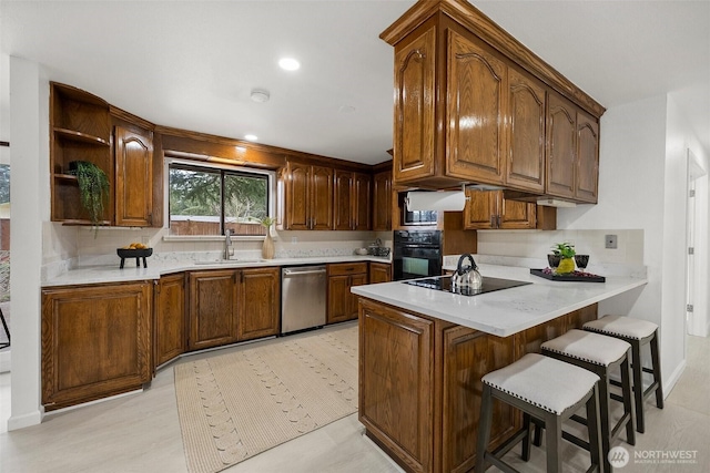 kitchen featuring a breakfast bar, a sink, light countertops, a peninsula, and black appliances