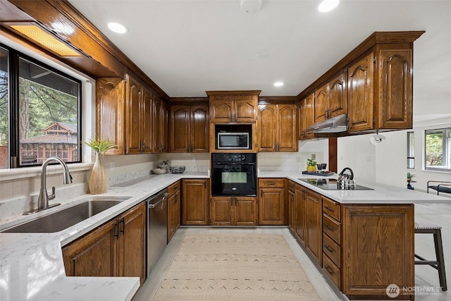 kitchen featuring a peninsula, a breakfast bar area, under cabinet range hood, a sink, and black appliances