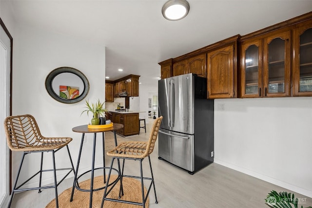 kitchen featuring freestanding refrigerator, glass insert cabinets, baseboards, light wood-type flooring, and light countertops