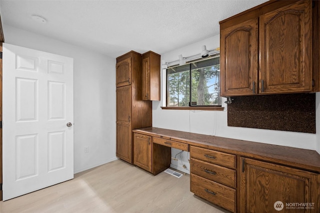 kitchen with a textured ceiling, visible vents, dark countertops, light wood-type flooring, and built in study area