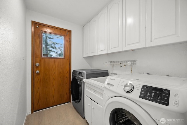 washroom with light wood-style flooring, cabinet space, and washing machine and clothes dryer