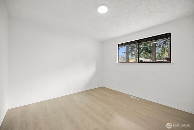 empty room featuring baseboards, a textured ceiling, wood finished floors, and visible vents