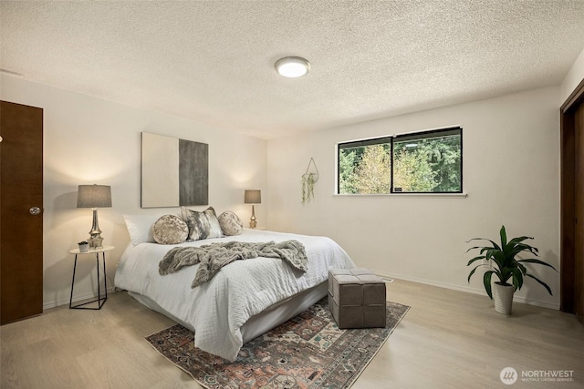 bedroom with a textured ceiling, baseboards, and light wood finished floors