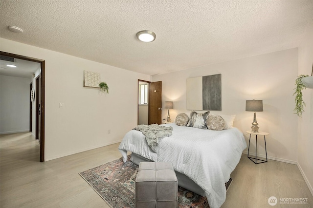 bedroom featuring baseboards, a textured ceiling, light wood-style flooring, and visible vents