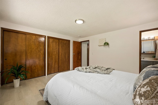 bedroom featuring multiple closets, light wood finished floors, a textured ceiling, and connected bathroom