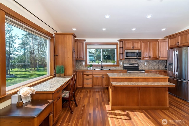 kitchen with wood finished floors, a center island, a sink, backsplash, and stainless steel appliances