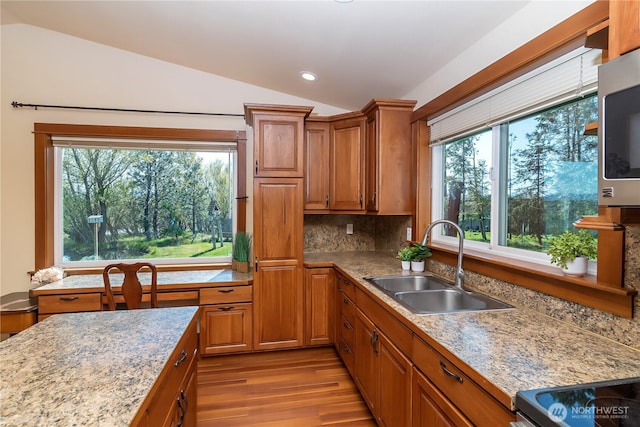 kitchen featuring a sink, light wood-style floors, vaulted ceiling, and brown cabinetry