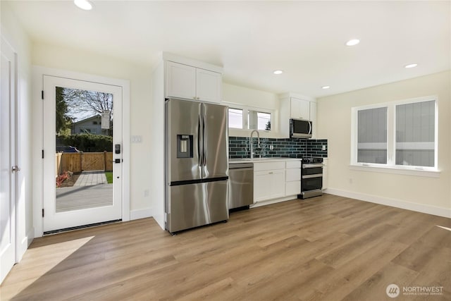 9253 6th Ave NW, Seattle, WA 98117 - kitchen with light wood-style floors, appliances with stainless steel finishes, white cabinets, and backsplash