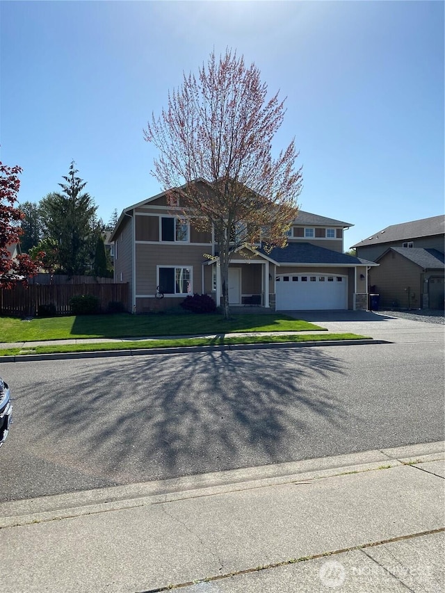 traditional-style home featuring aphalt driveway, fence, a front yard, and a garage