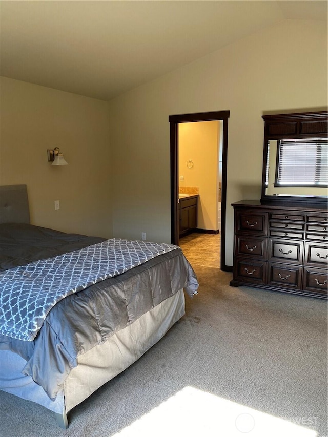 bedroom featuring connected bathroom, vaulted ceiling, and light carpet