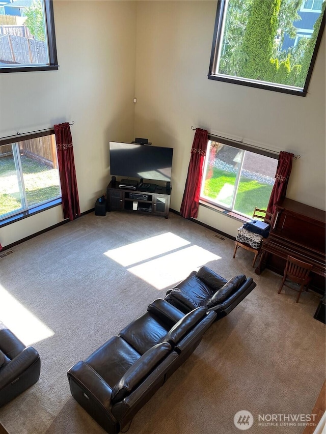 living room featuring carpet flooring, a high ceiling, visible vents, and a wealth of natural light