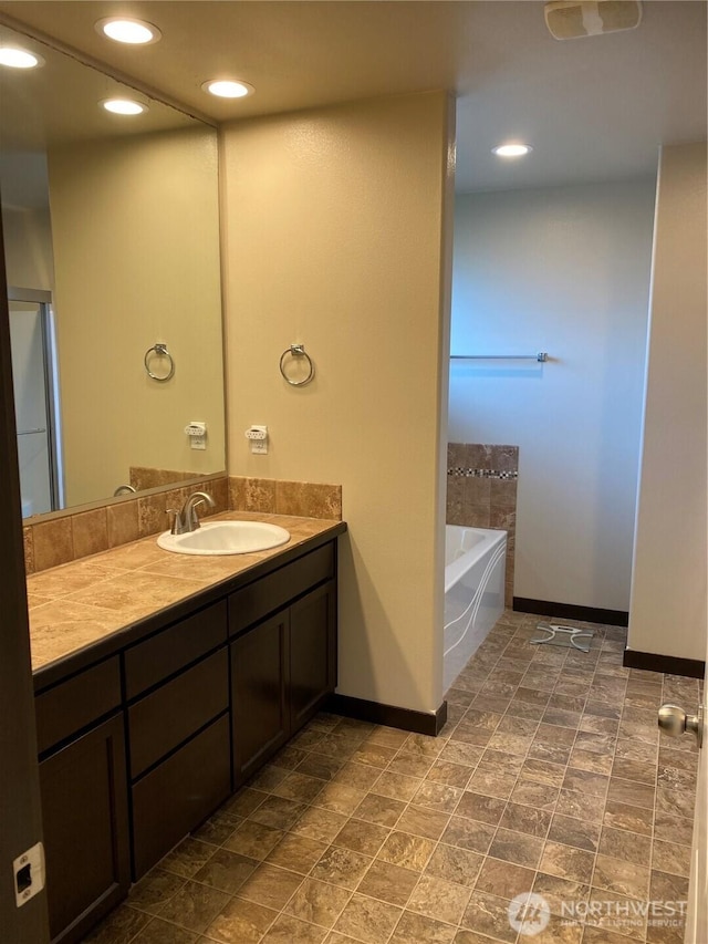 full bath featuring vanity, recessed lighting, baseboards, and a garden tub