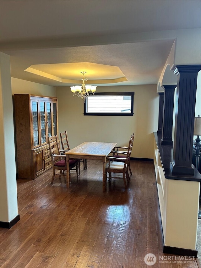 dining space featuring baseboards, a tray ceiling, dark wood-style flooring, and a notable chandelier