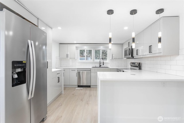 kitchen featuring appliances with stainless steel finishes, modern cabinets, a sink, a peninsula, and light wood-style floors