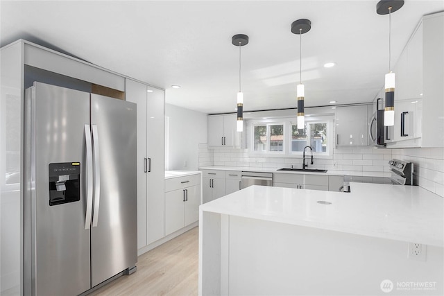 kitchen with a sink, light wood-style flooring, stainless steel appliances, a peninsula, and backsplash