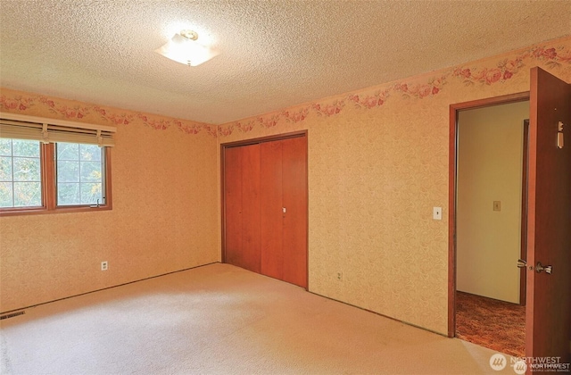 unfurnished bedroom with carpet floors, a textured ceiling, visible vents, and a closet