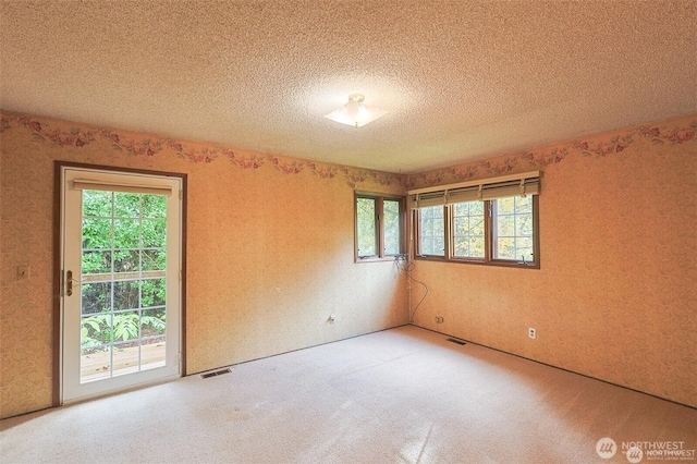 unfurnished room featuring a textured ceiling, wallpapered walls, visible vents, and carpet