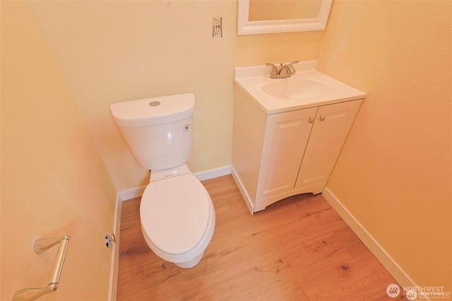 half bath with vanity, baseboards, wood finished floors, and toilet