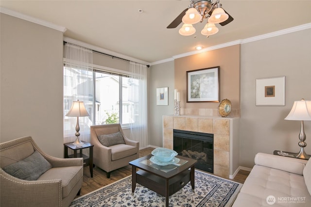 living room featuring a ceiling fan, crown molding, a tiled fireplace, wood finished floors, and baseboards