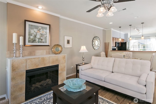 living room with crown molding, ceiling fan, baseboards, wood finished floors, and visible vents
