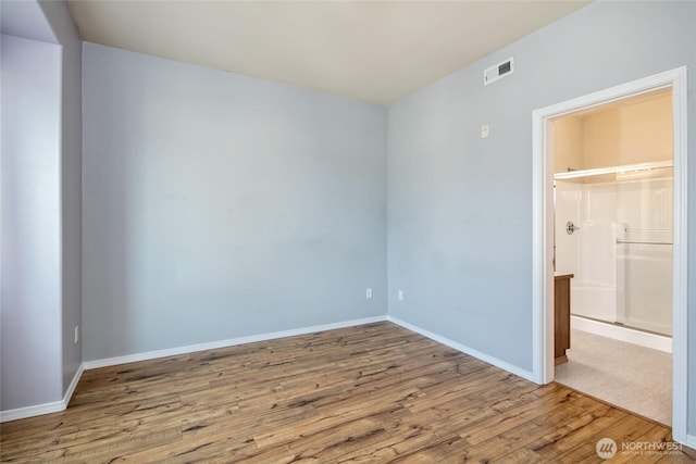 unfurnished bedroom featuring connected bathroom, baseboards, visible vents, and wood finished floors