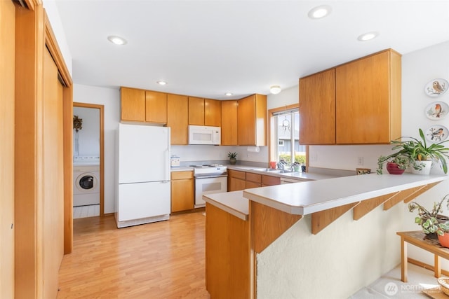 kitchen featuring washer / dryer, a peninsula, white appliances, light countertops, and light wood finished floors