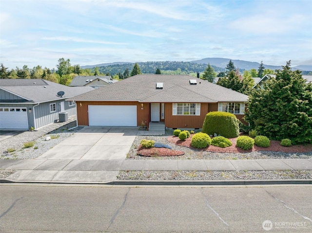 ranch-style home with roof with shingles, central air condition unit, a mountain view, concrete driveway, and an attached garage
