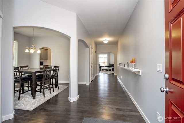 foyer featuring arched walkways, dark wood-style flooring, a chandelier, and baseboards