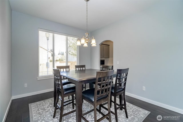 dining area featuring arched walkways, baseboards, dark wood-style floors, and a chandelier