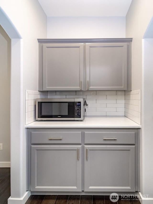 bar with stainless steel microwave, tasteful backsplash, baseboards, and dark wood-style floors