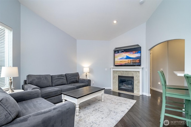 living room with dark wood-type flooring, baseboards, a tile fireplace, arched walkways, and vaulted ceiling