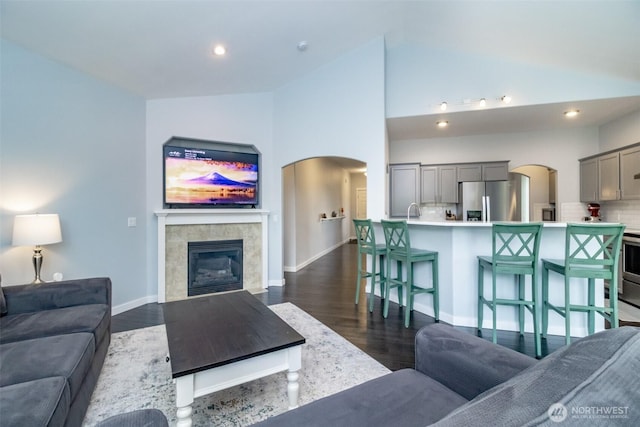 living area with arched walkways, baseboards, dark wood-style floors, recessed lighting, and high vaulted ceiling