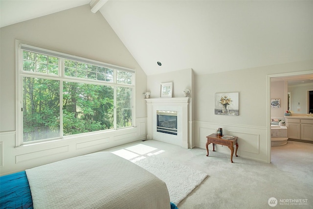 bedroom with a glass covered fireplace, a decorative wall, light colored carpet, a wainscoted wall, and lofted ceiling with beams