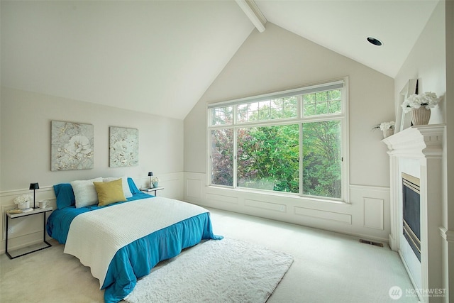 bedroom featuring a wainscoted wall, visible vents, lofted ceiling with beams, and light colored carpet