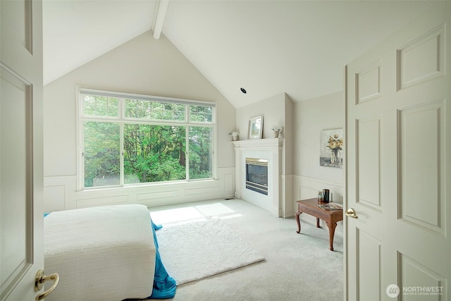 bedroom featuring a glass covered fireplace, light colored carpet, lofted ceiling with beams, and a wainscoted wall