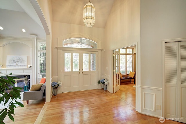 entrance foyer featuring light wood-type flooring, a fireplace, a notable chandelier, and high vaulted ceiling
