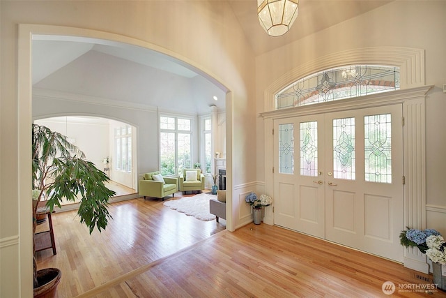 foyer entrance with french doors, a towering ceiling, arched walkways, wood finished floors, and a wainscoted wall